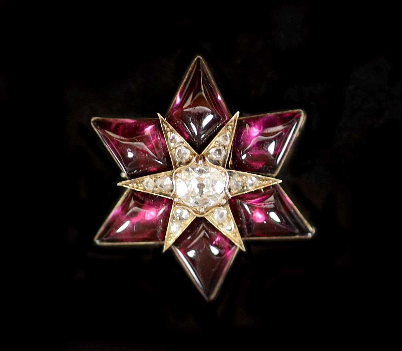 An early 19th century gold, shaped cabochon garnet, cushion cut diamond and graduated rose cut diamond set star brooch